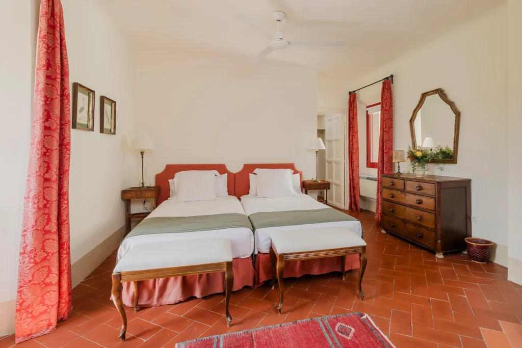Habitación doble con muebles clásicos y cortinas rojas en el Castell de Sant Mori